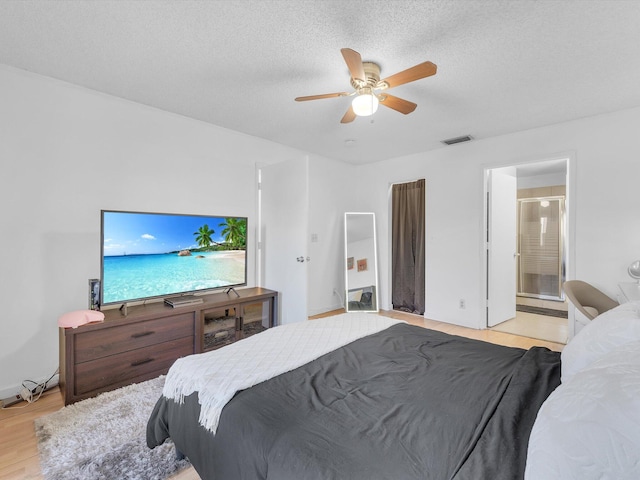 bedroom with a textured ceiling, light wood-type flooring, ensuite bathroom, and ceiling fan