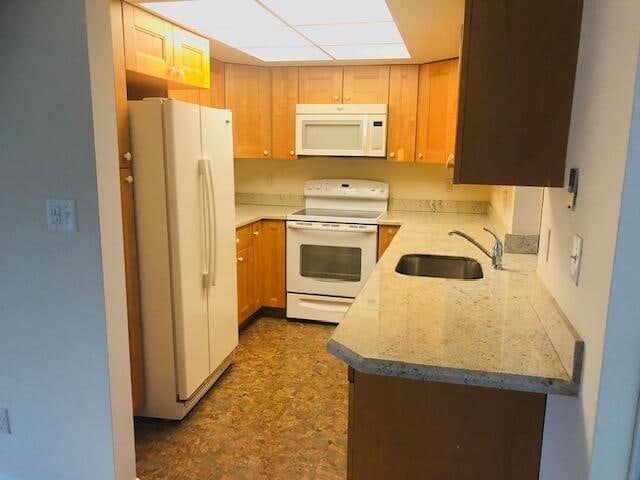 kitchen featuring light stone countertops, white appliances, and sink