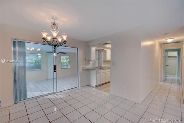 tiled empty room with ceiling fan with notable chandelier