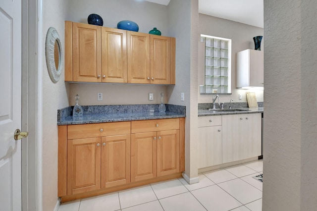 kitchen featuring light tile patterned floors, dark stone counters, and sink