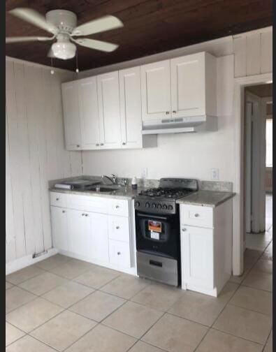 kitchen featuring gas stove, wood walls, sink, white cabinets, and ceiling fan