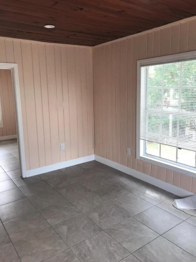 tiled empty room featuring wood walls, a wealth of natural light, and wooden ceiling