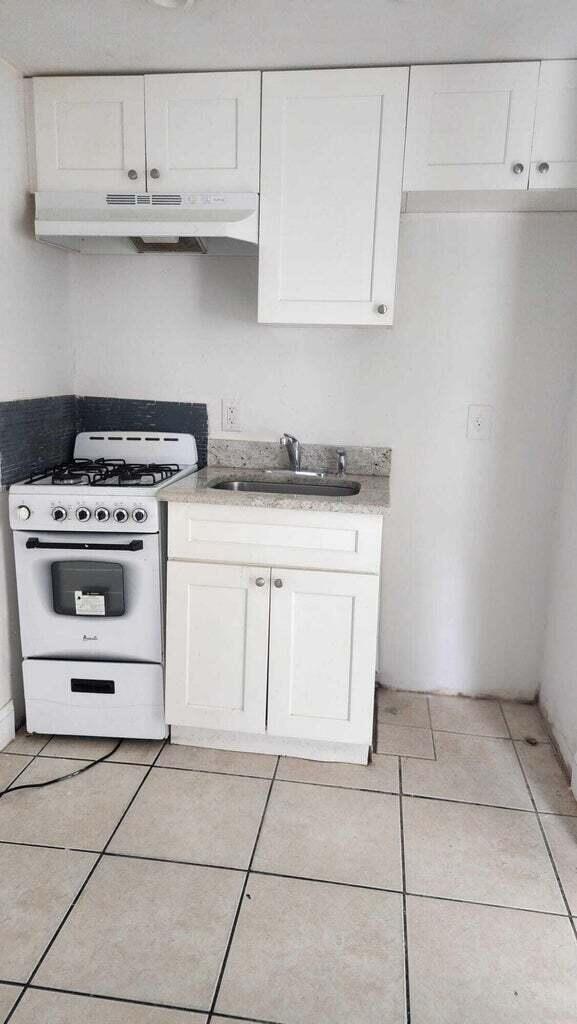 kitchen with white cabinetry, sink, white gas range, and light tile patterned flooring