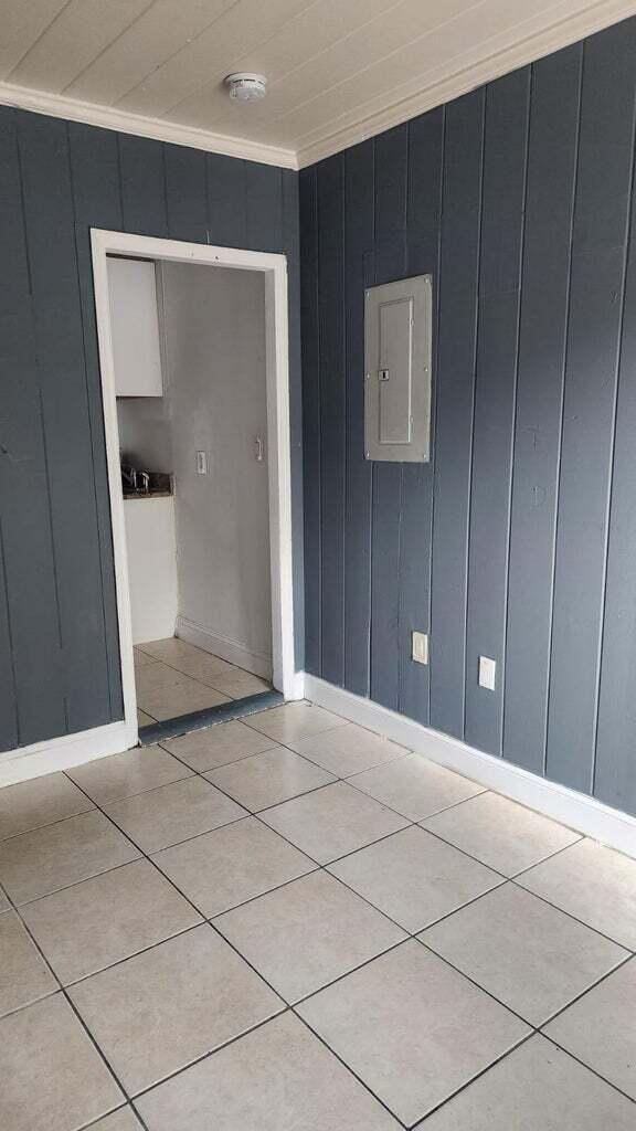 tiled empty room featuring ornamental molding, electric panel, and wood walls