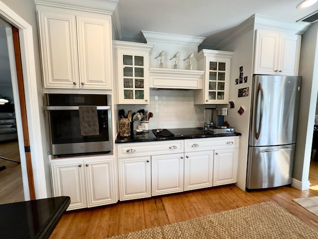 kitchen with white cabinets, appliances with stainless steel finishes, light wood-type flooring, and backsplash