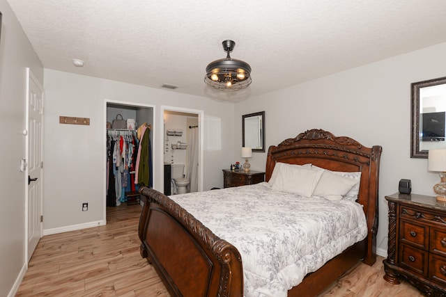 bedroom with connected bathroom, a spacious closet, a textured ceiling, a closet, and light wood-type flooring