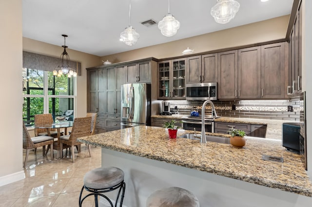 kitchen with stainless steel appliances, dark brown cabinetry, light stone countertops, hanging light fixtures, and decorative backsplash