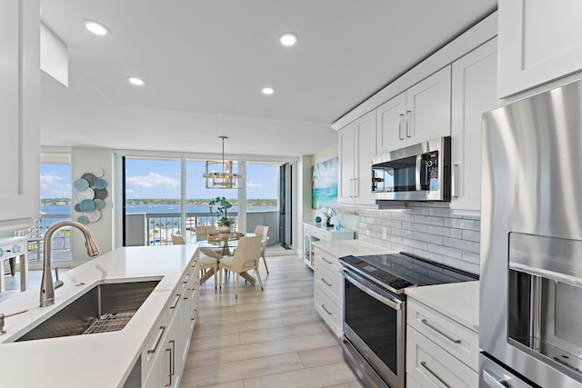 kitchen with backsplash, stainless steel appliances, sink, a water view, and white cabinetry