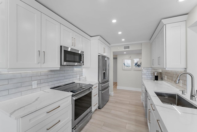 kitchen featuring light stone countertops, white cabinetry, sink, stainless steel appliances, and decorative backsplash