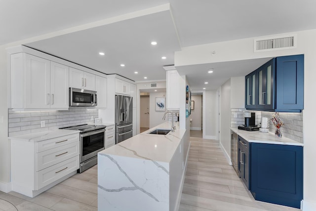 kitchen featuring blue cabinets, sink, decorative backsplash, light stone countertops, and appliances with stainless steel finishes