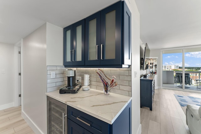 kitchen featuring decorative backsplash, light stone countertops, blue cabinets, light hardwood / wood-style floors, and wine cooler