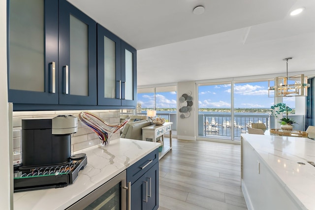 kitchen with a water view, blue cabinets, hanging light fixtures, light wood-type flooring, and light stone countertops