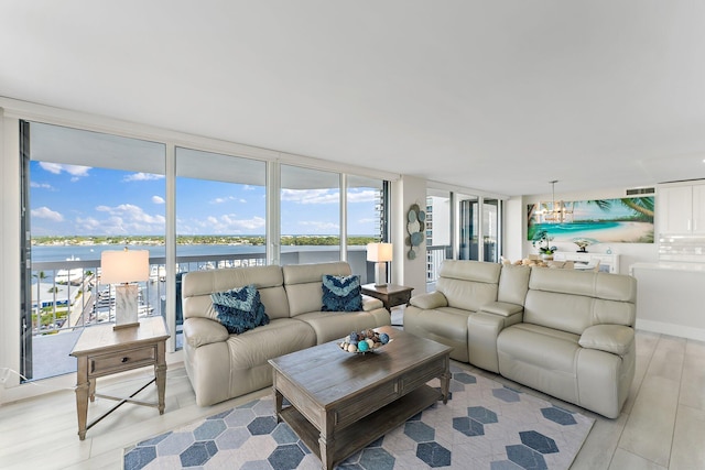 living room with a chandelier, light hardwood / wood-style floors, a wall of windows, and a water view