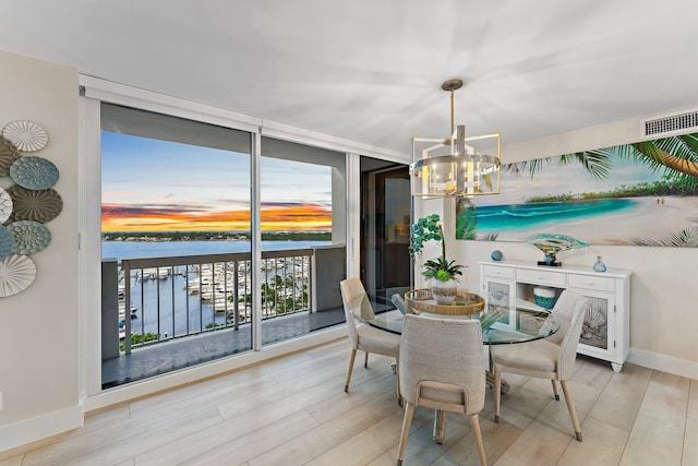 dining space with an inviting chandelier, a water view, and light hardwood / wood-style flooring