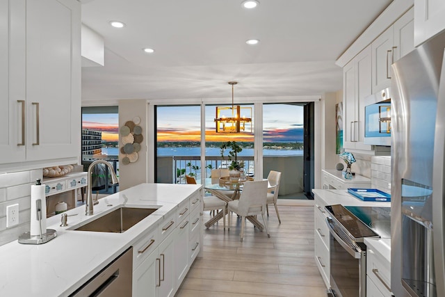 kitchen with appliances with stainless steel finishes, backsplash, sink, decorative light fixtures, and white cabinetry