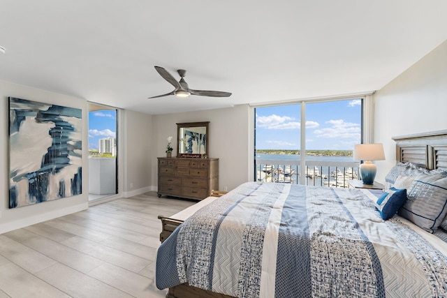 bedroom with access to exterior, light wood-type flooring, floor to ceiling windows, ceiling fan, and a water view