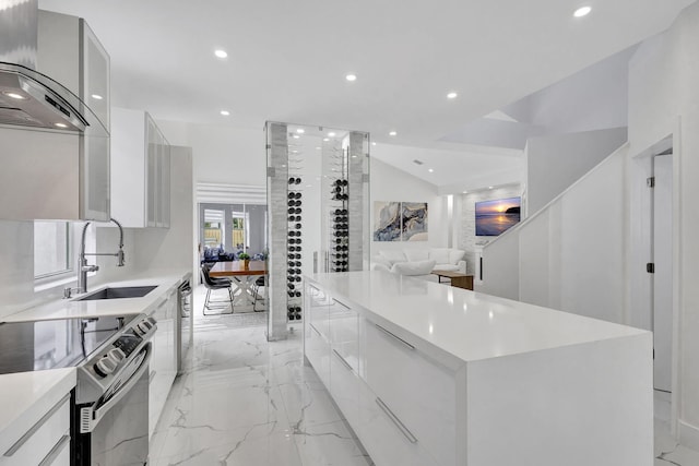 kitchen featuring sink, stainless steel range with electric cooktop, a kitchen island, white cabinets, and wall chimney range hood