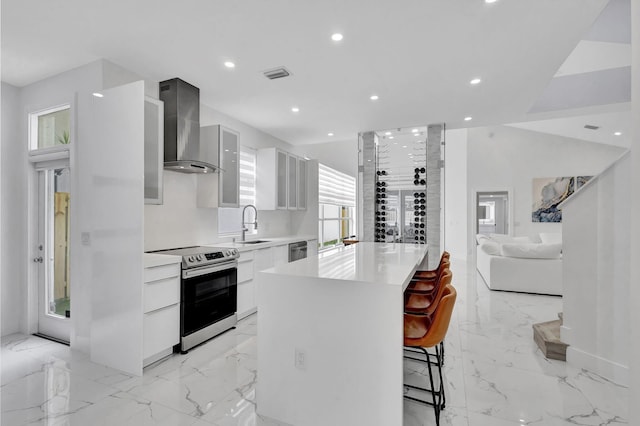 kitchen featuring a center island, white cabinets, a breakfast bar area, wall chimney range hood, and appliances with stainless steel finishes