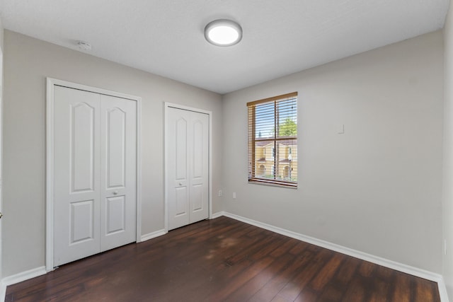 unfurnished bedroom featuring two closets and dark wood-type flooring