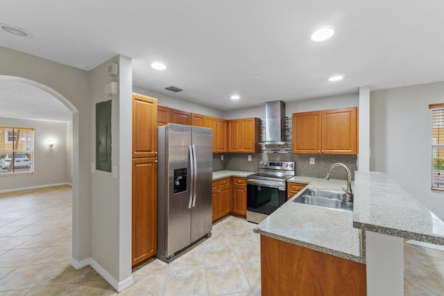 kitchen with kitchen peninsula, appliances with stainless steel finishes, backsplash, sink, and wall chimney range hood