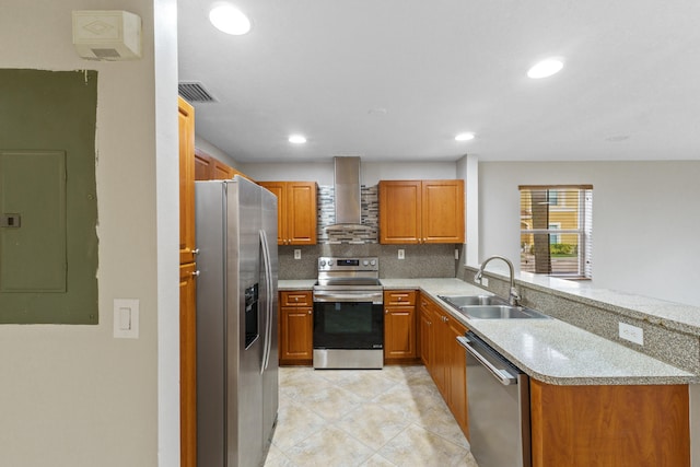 kitchen featuring sink, wall chimney exhaust hood, light stone countertops, appliances with stainless steel finishes, and kitchen peninsula