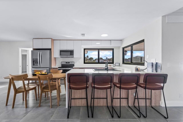 kitchen with stainless steel appliances, kitchen peninsula, sink, a breakfast bar area, and white cabinetry