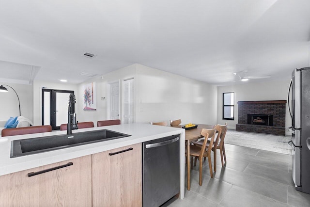 kitchen with stainless steel appliances, sink, light brown cabinetry, ceiling fan, and a fireplace