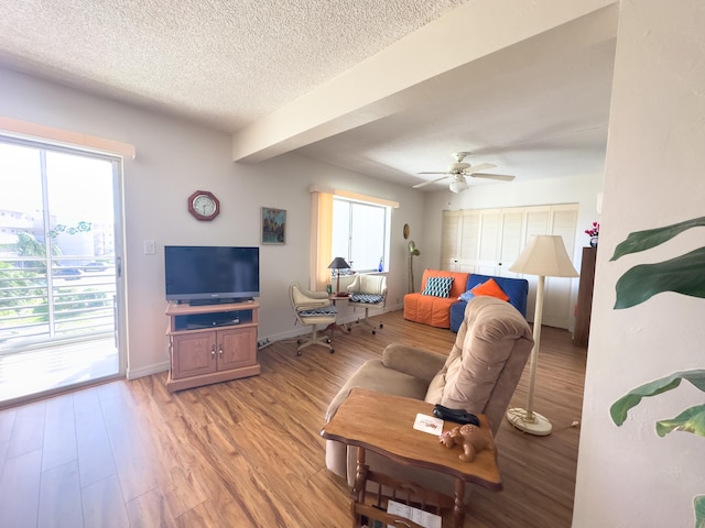 living room featuring beam ceiling, ceiling fan, light hardwood / wood-style flooring, and a textured ceiling