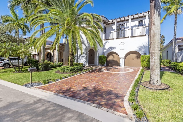 mediterranean / spanish house featuring a balcony, a tiled roof, a front lawn, and stucco siding