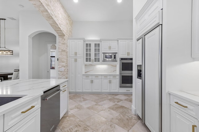 kitchen featuring arched walkways, white cabinets, glass insert cabinets, light stone counters, and built in appliances