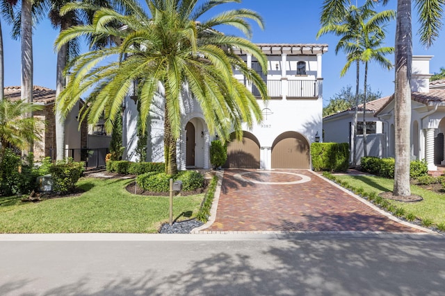 mediterranean / spanish house featuring a tiled roof, a front lawn, decorative driveway, and stucco siding