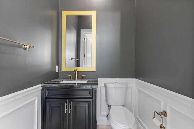 half bath featuring a wainscoted wall, a decorative wall, vanity, and toilet