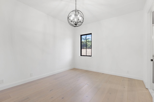 empty room with light wood-type flooring, a notable chandelier, and baseboards