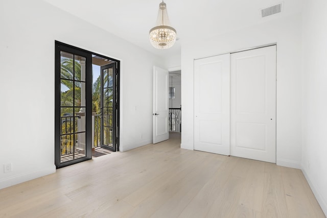 unfurnished room with baseboards, visible vents, a chandelier, and wood finished floors