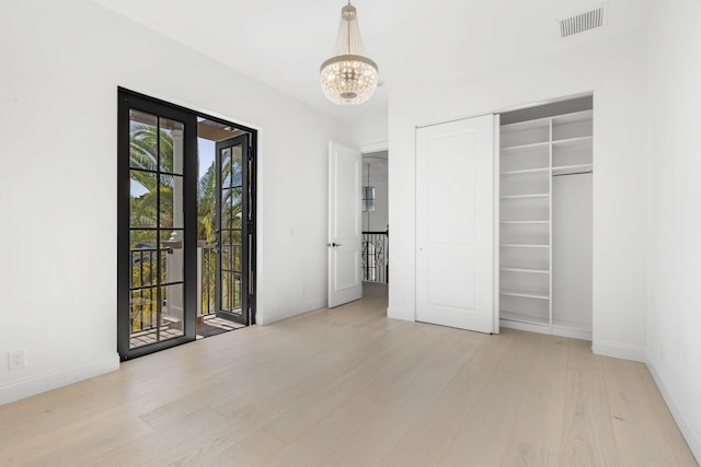 unfurnished bedroom with visible vents, wood finished floors, access to exterior, a chandelier, and a closet