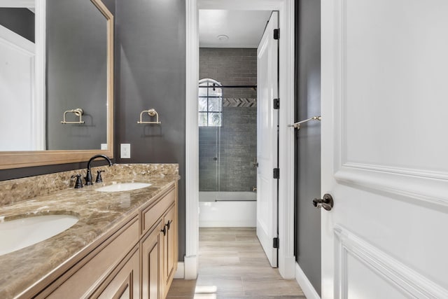 bathroom featuring double vanity, tub / shower combination, a sink, and wood finished floors