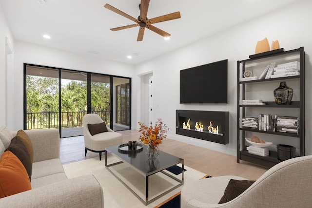 living area with a lit fireplace, wood finished floors, a ceiling fan, and recessed lighting