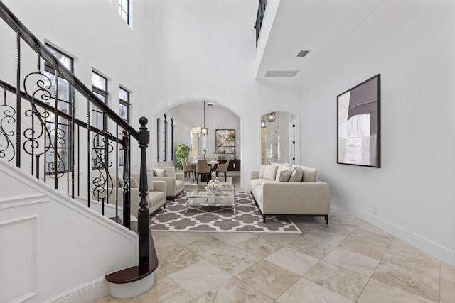 entrance foyer with arched walkways, a towering ceiling, visible vents, baseboards, and stairway