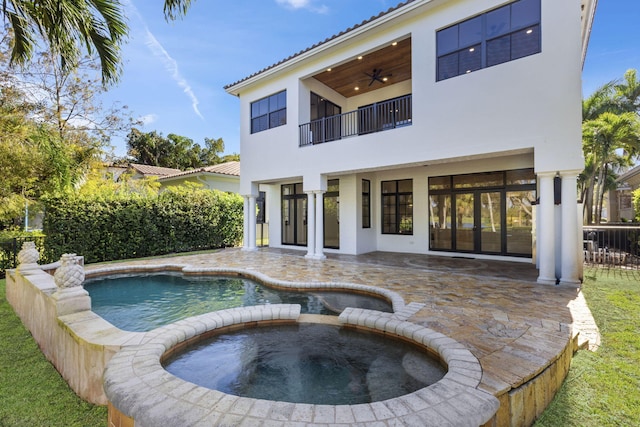 rear view of house with a patio, a balcony, an in ground hot tub, a ceiling fan, and stucco siding