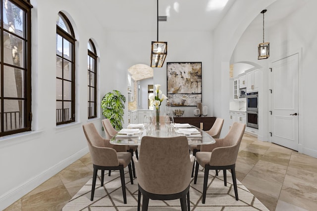 dining space with a towering ceiling, visible vents, baseboards, and arched walkways