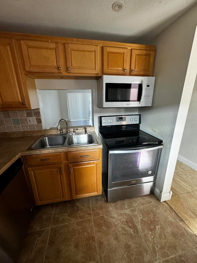 kitchen featuring tasteful backsplash, a textured ceiling, stainless steel appliances, sink, and dark tile patterned flooring