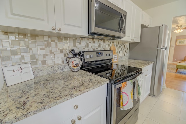 kitchen featuring light stone counters, stainless steel appliances, white cabinetry, light tile patterned floors, and decorative backsplash