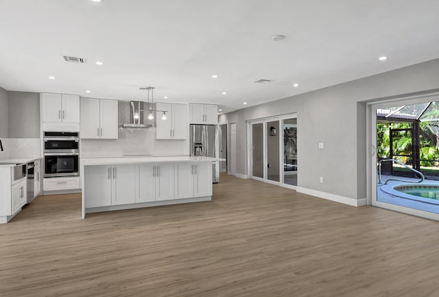 kitchen with white cabinets, wall chimney range hood, pendant lighting, and appliances with stainless steel finishes