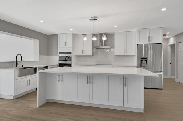 kitchen featuring stainless steel appliances, white cabinets, wall chimney exhaust hood, hanging light fixtures, and light wood-type flooring