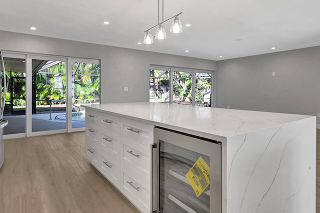 kitchen with beverage cooler, white cabinets, light stone counters, and plenty of natural light