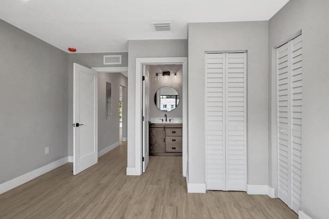 unfurnished bedroom featuring ensuite bathroom, sink, and light wood-type flooring