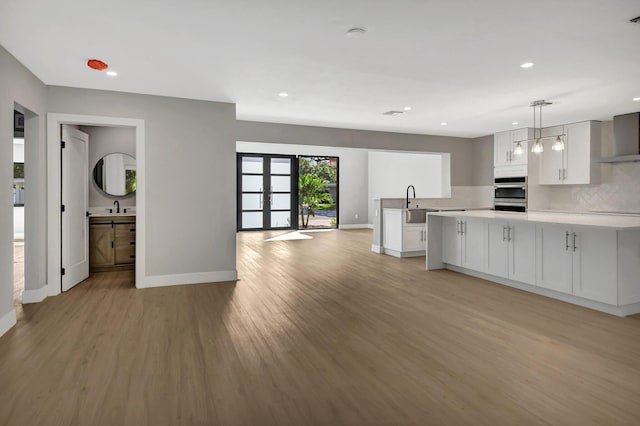 kitchen featuring white cabinets, light wood-type flooring, hanging light fixtures, and double oven