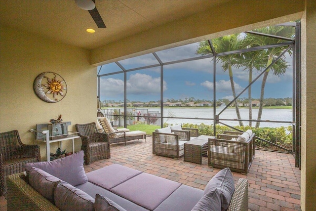 view of patio / terrace featuring a water view, glass enclosure, ceiling fan, and an outdoor living space