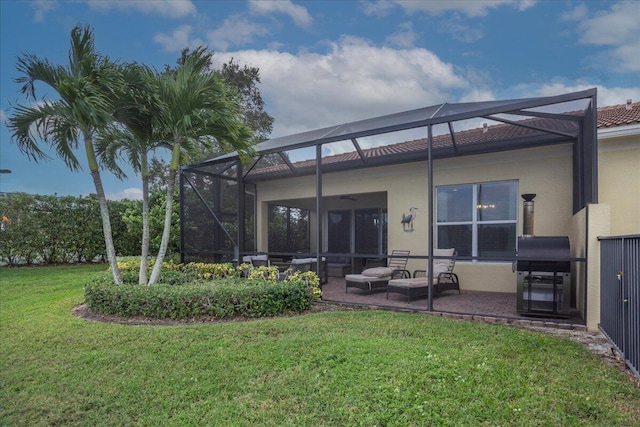 rear view of house with glass enclosure, a tile roof, a yard, stucco siding, and a patio area