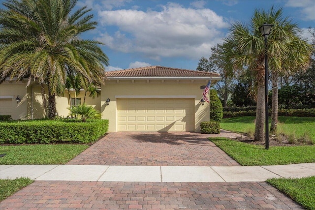 mediterranean / spanish home featuring a garage, a tiled roof, decorative driveway, and stucco siding